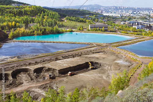 View on ash collectors of Thermal power plant in the quarry Uval Promarteli. Dirty water with bright blue color stored in specialized ash pond reservoirs. Excavator with dump trucks work in a career