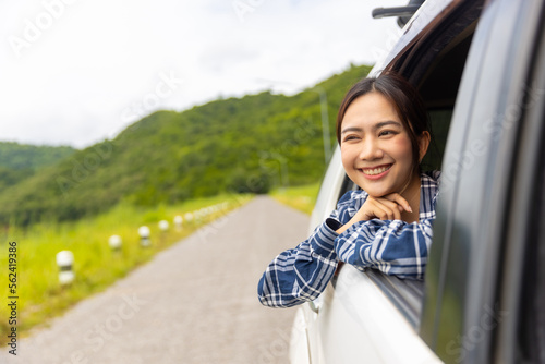 Young Asian woman enjoy outdoor lifestyle road trip and camping in forest mountain on summer travel vacation. Happy attractive girl sitting in driving car with pull her face and hand out of car window