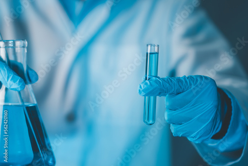 Fotografie Scientist hand hold test tubes and erlenmeyer flask filled with blue sample chemicals in chemistry science laboratory