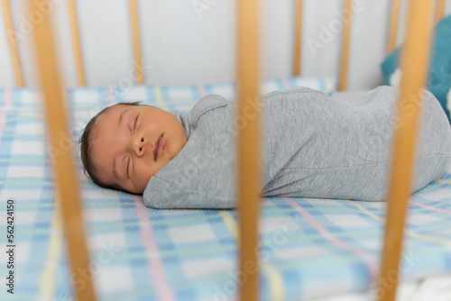 The baby is lying in a cocoon on cot. He sleeps sweetly and dreams.