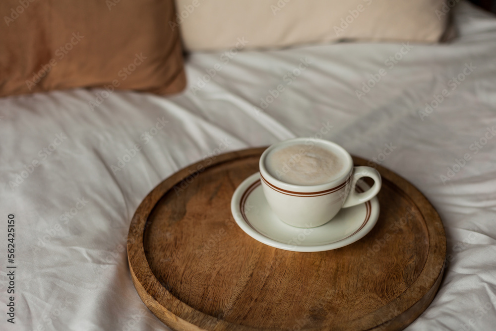 Hot mug of cappuccino on wooden tray on the bed, breakfast. Cozy house. Beige natural colors. Aesthetic.