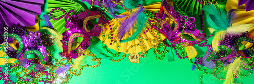 Mardi Gras colourful holiday greeting card background with festival masquerade accessories, decor, carnival mask, beads, feathers, fan on bright background traditional yellow purple green colors