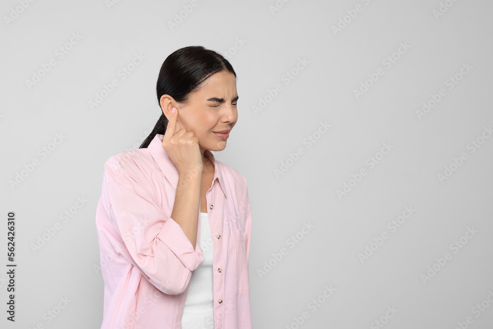 Young woman suffering from ear pain on light grey background. Space for text Young woman suffering from ear pain on light grey background. Space for text