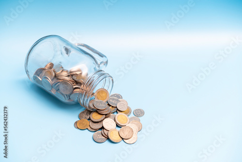 A lot of money coin flow out of the glass jar on blue background, Saving money concept.