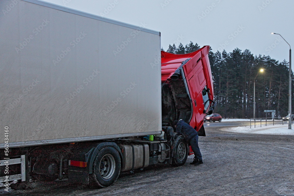 Heavy red semi truck with trailer diesel engine repair under opened cab hood at cold winter snowy road