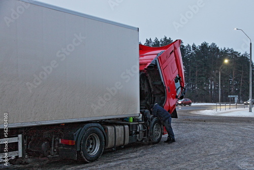 Obraz na płótnie Heavy red semi truck with trailer diesel engine repair under opened cab hood at cold winter snowy road w salonie