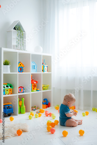 baby 7-9 months to a year old sits on the floor in a cozy white interior nursery with stylish furniture © shangarey