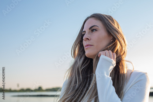 portrait of a beautiful young Women on a beach with sunlight and water in background laughing ans looking over the sea with hand in her hair