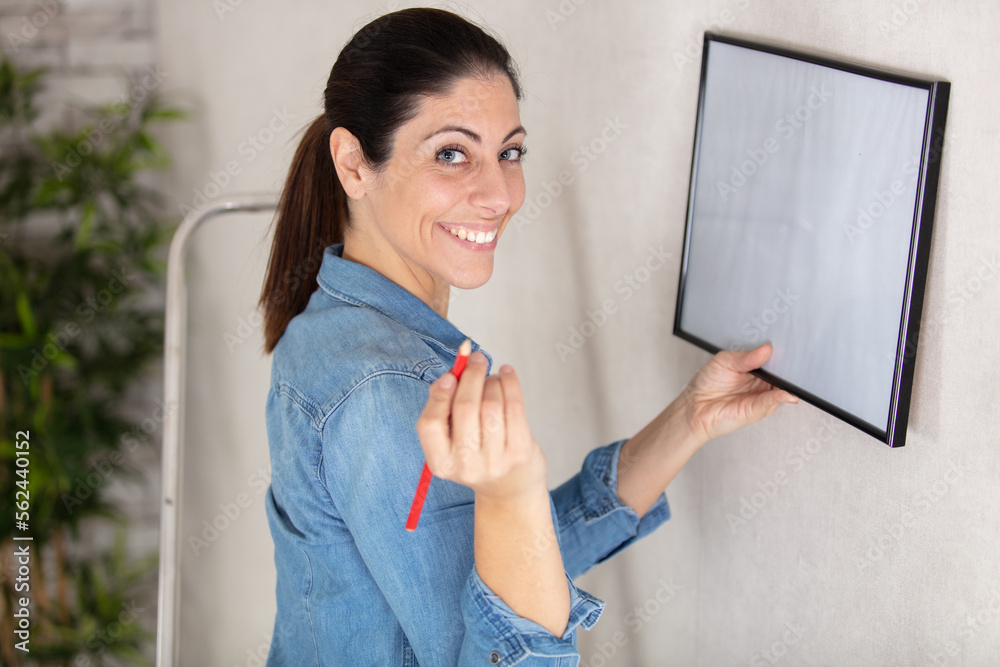 young woman putting photo frame on white wall young woman putting photo frame on white wall