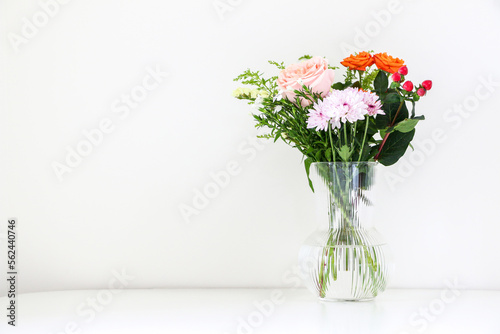Beautiful bouquet of flowers with pink and orange roses and white chrysanthemum, on right of white table against white background, with copy space © Adam