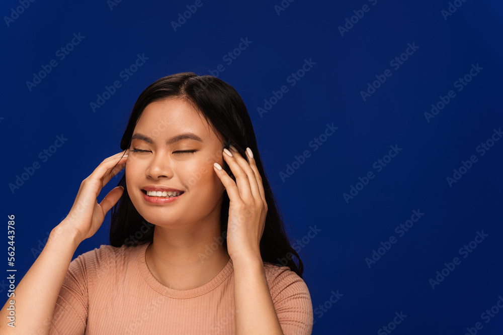 Pretty asian woman in t-shirt touching head isolated on blue Pretty asian woman in t-shirt touching head isolated on blue