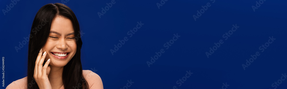 Cheerful asian woman closing eyes isolated on blue, banner Cheerful asian woman closing eyes isolated on blue, banner