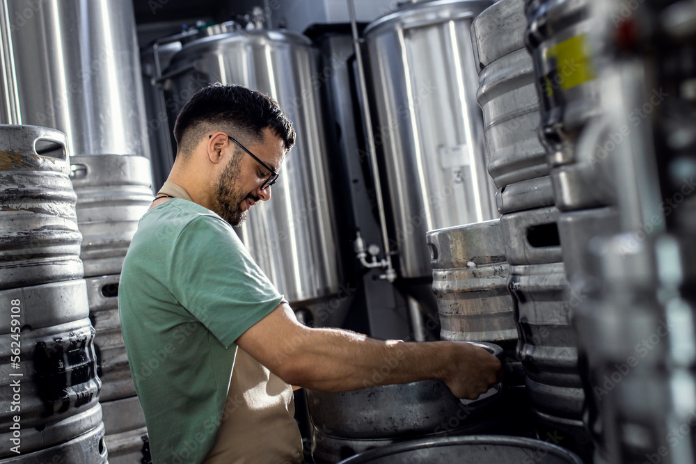Man working in craft brewery examining production of the beer. Man working in craft brewery examining production of the beer.