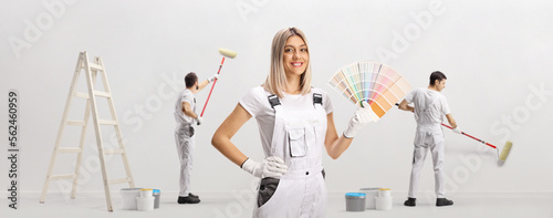 Female house painter holding a color palette and male workers painting a wall photo