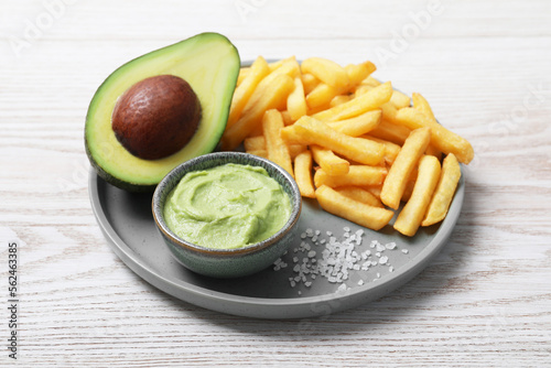 Plate with french fries, guacamole dip and avocado served on white wooden table