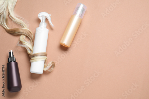 Spray bottles with thermal protection and lock of blonde hair on beige background, flat lay. Space for text