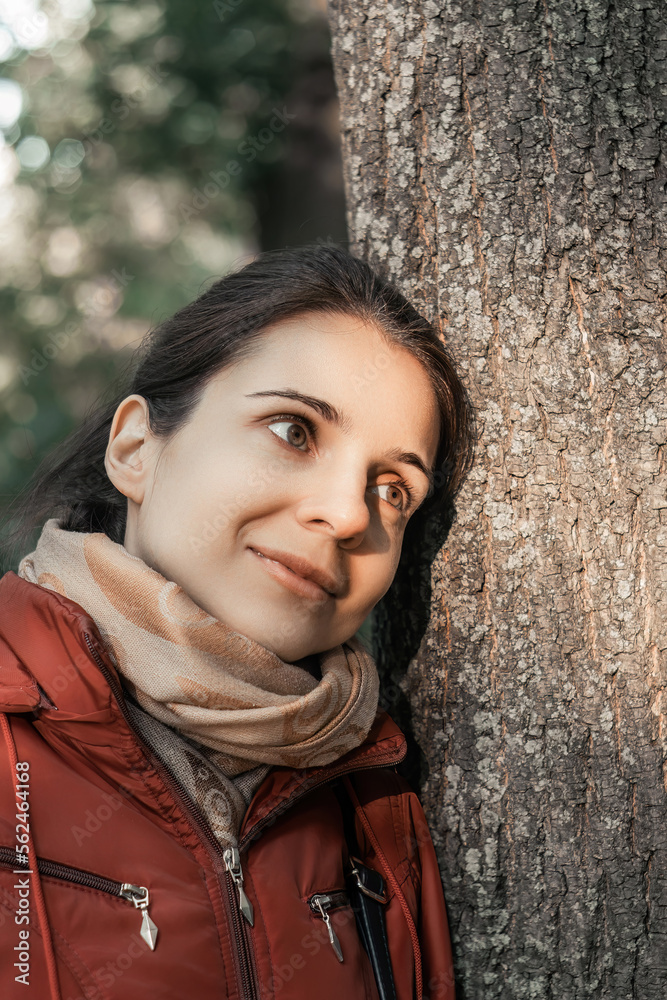 Portrait of young woman leaning against tree trunk
