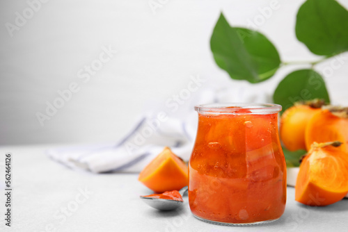 Fototapeta Naklejka Na Ścianę i Meble -  Jar of tasty persimmon jam, ingredients on white table. Space for text