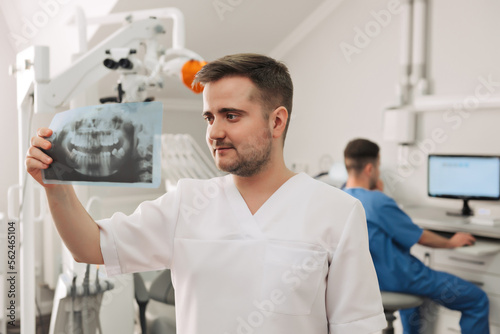 picture of male doctor or dentist looking at x-ray with his assistant on the background