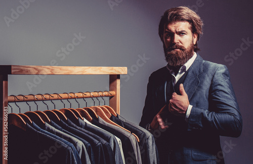 Male suits hanging in a row. Men clothing, boutiques. Handsome bearded fashion man in classical costume suit photo