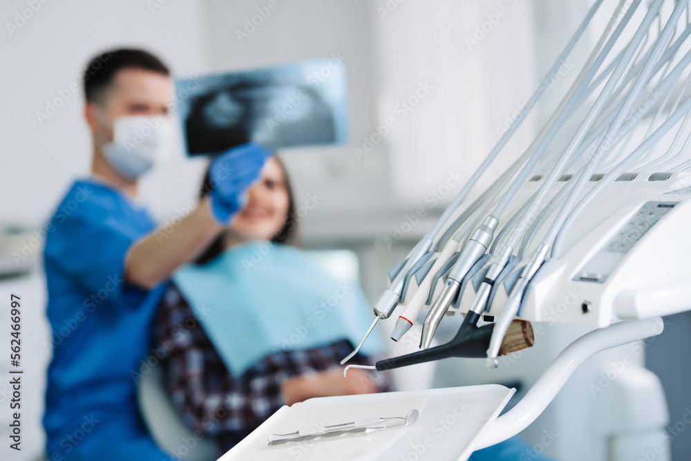 Dental instruments with dentist and patient looking at x-ray on background.