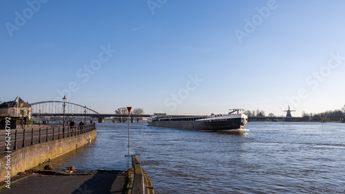 Empty barge sails downstream during high tide of the river IJssel past the Hanseatic city of Deventer in the Netherlands © Ton