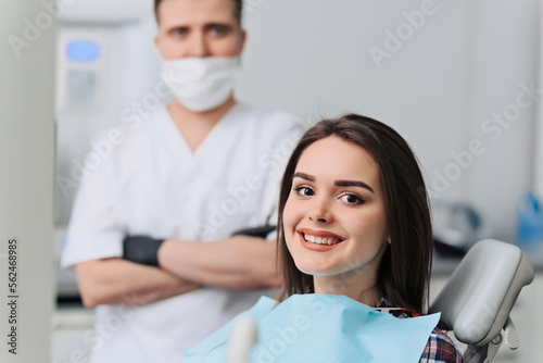 Satisfied dentist patient showing her perfect smile after treatment in a clinic box with dentist in the background