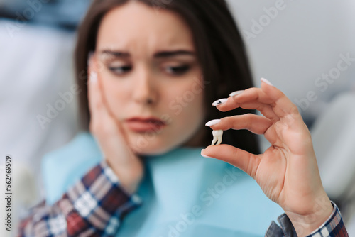 Young woman has toothache. concept for healthy care. Female patient holding tooth model in hands in dentist office.