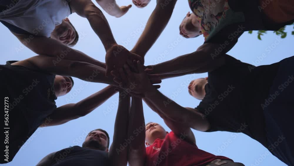 Young athletes stacking their hands together one by one in unity. Group of best friends putting their arms in centre of a circle and raising them up to the blue sky. Friendship and teamwork concept
