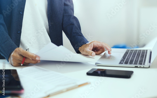 Asian businessman in casual cloth using laptop computer working from home and reviewing business contract while he meeting online with business group