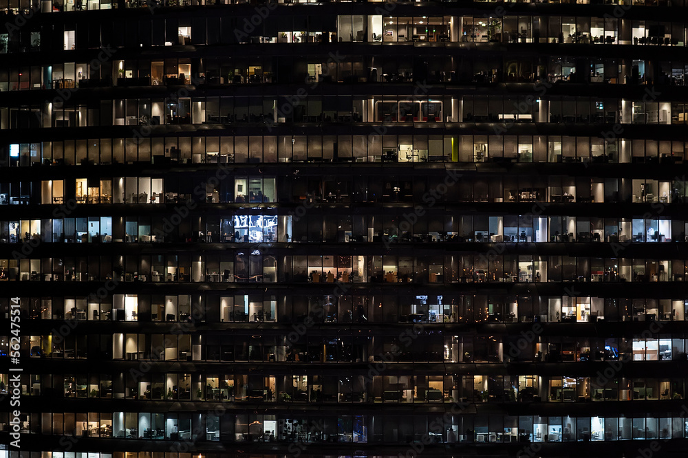 Frontal view of the night facade of building with a lot of windows with light. life in every window. night view of the glass facade of an office skyscraper. Frontal view of the night facade of building with a lot of windows with light. life in every window. night view of the glass facade of an office skyscraper.