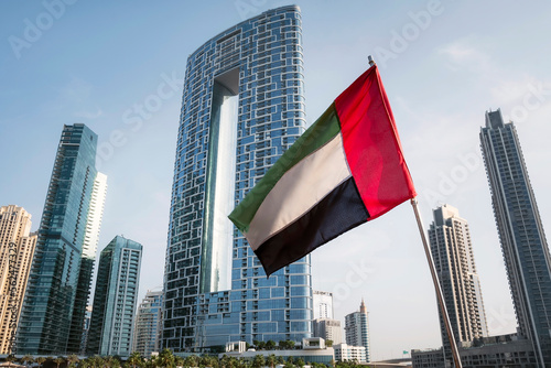 view of UAE, United Arab Emirates national flag waving in the air with Dubai skyline in background. UAE National Day