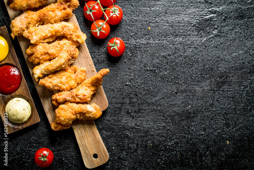 Chicken strips on a cutting Board with different sauces and tomatoes.
