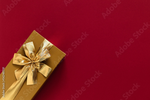Golden gift box with golden ribbon and bow on a burgundy background. Top view. Copy space.