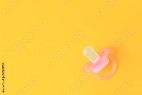 One new baby pacifier on orange background, top view. Space for text