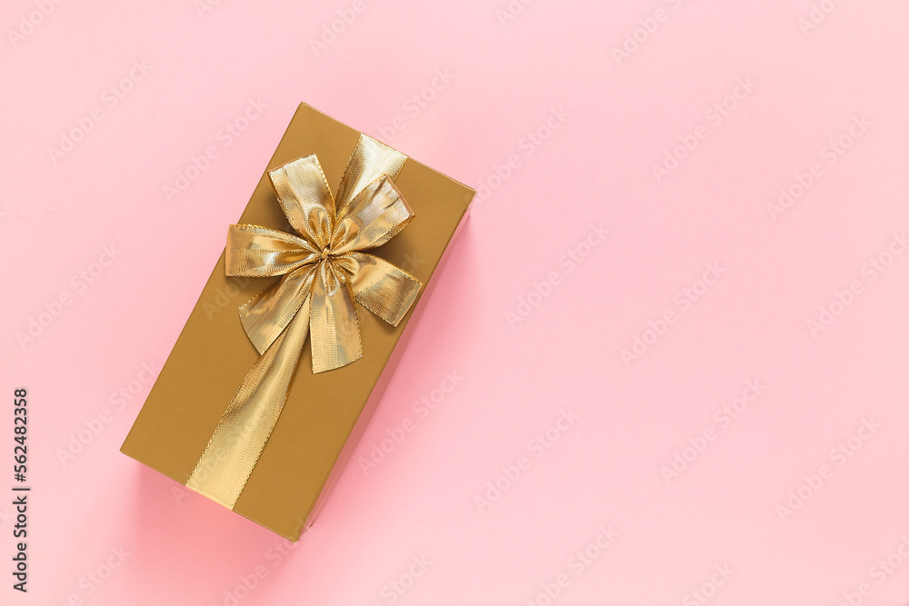 Golden gift box with golden ribbon and bow on a pink background. Top view. Copy space. Golden gift box with golden ribbon and bow on a pink background. Top view. Copy space.