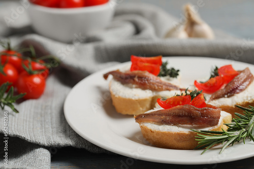 Delicious sandwiches with cream cheese, anchovies and tomatoes on grey wooden table, closeup. Space for text