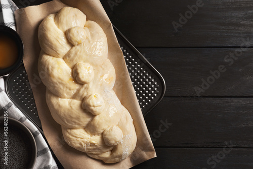 Raw braided bread and ingredients on black wooden table, flat lay with space for text. Traditional Shabbat challah photo