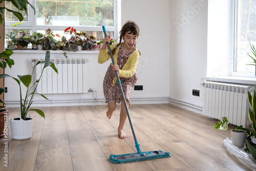 A girl dances with a mop to clean the floor in a new house - general cleaning in an empty room, the joy of moving, help with the housework