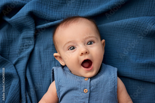 Portrait of funny newborn baby lying on blue blanket making surprised face photo