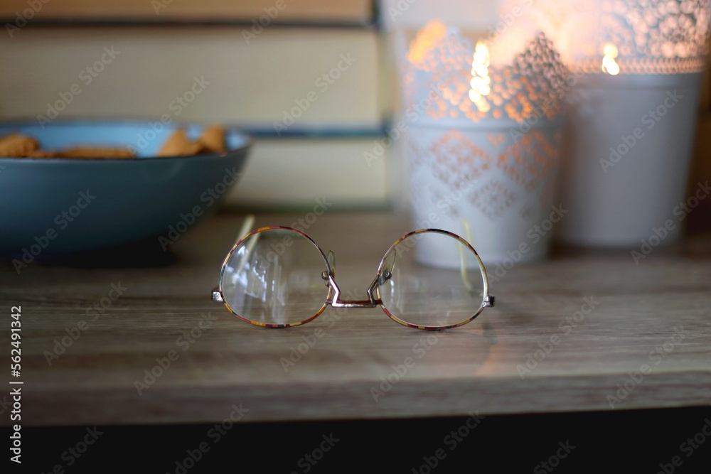 Glasses, bowl of biscuits, lit candles and books in the background. Selective focus.