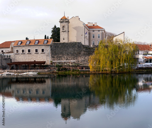 Herzegovina museum also known as Muzej Hercegovine in old town of Trebinje with stone fortress wall and tall tower under water surface of Trebisnjica river autumn landscape front view