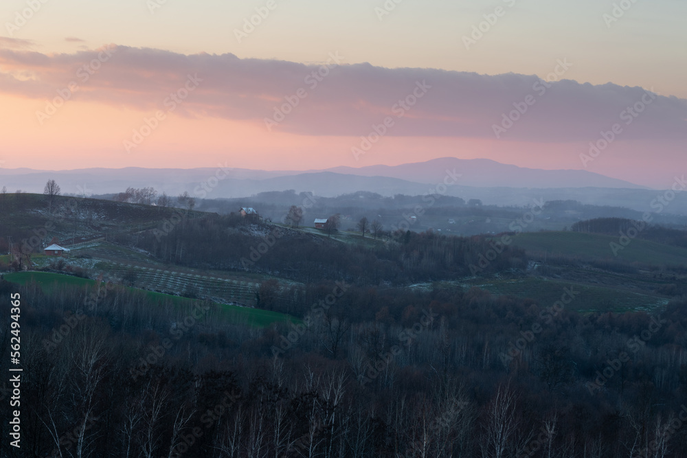 Hilly village against mountain silhouette at dusk, peaceful rural landscape in winter Hilly village against mountain silhouette at dusk, peaceful rural landscape in winter
