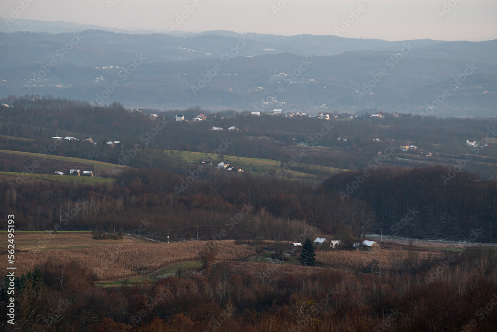 Peaceful hilly village panorama at dusk, first snow on house rooftops, lovely evening in countryside
