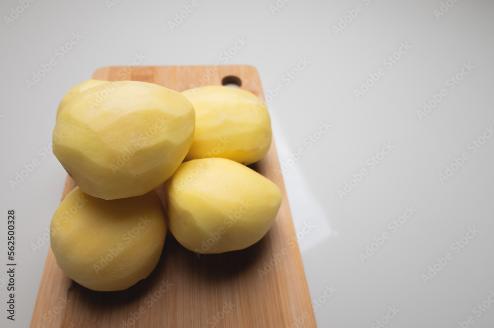 Peeled fresh classic frying potatoes on a wooden cutting board on a white table