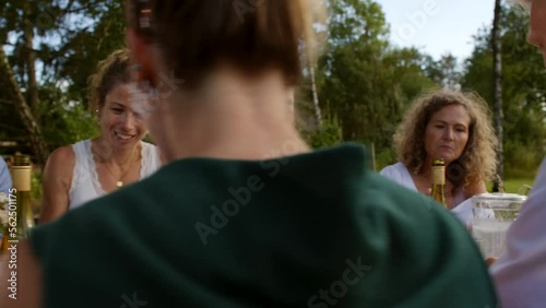 Smiling family and friends talking over wine and a meal together outside around a table in summer