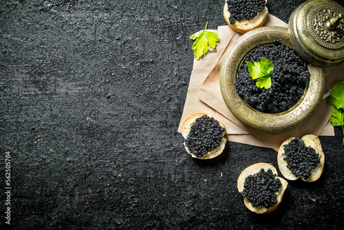 Black caviar on bread slices and caviar in a bowl on paper with parsley.