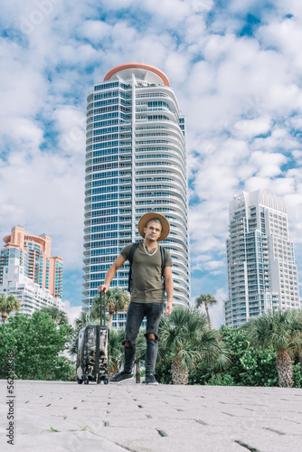 Full body portrait of smiling handsome man walking outside with suitcase