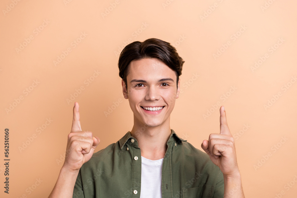 Portrait of friendly candid person beaming smile direct fingers up empty space isolated on beige color background Portrait of friendly candid person beaming smile direct fingers up empty space isolated on beige color background