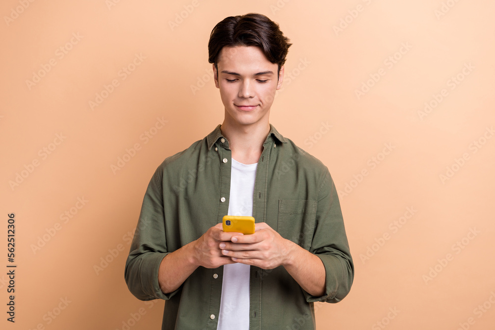 Photo of young student brunet hair man wear khaki stylish shirt chatting online use new phone new convenient app isolated on beige color background Photo of young student brunet hair man wear khaki stylish shirt chatting online use new phone new convenient app isolated on beige color background